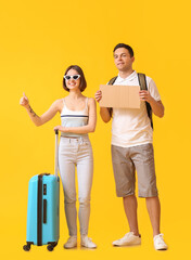 Young couple with cardboard and suitcase hitchhiking on color background