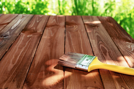 Wood staining diy. Brush. Painting wooden patio deck with protective brown oak varnish. Outdoors garden. Decking works