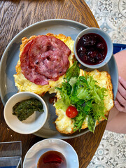 Half Cut Croissant Sandwich with Bacon, Scrambled Egg, Pesto Sauce and Marmalade Jam in Breakfast Plate.