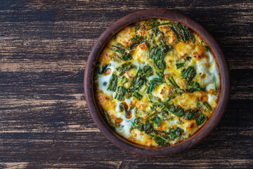 Ceramic bowl with vegetable frittata, simple vegetarian food. Frittata with egg, pepper, onion, cheese and green wild garlic leaves on table