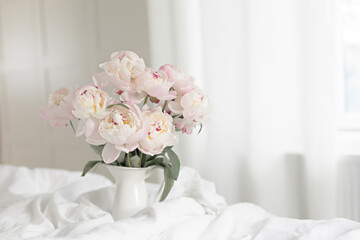 Bouquet of pink peonies on white bed linen. Modern interior in the bedroom. Wedding and festive style.