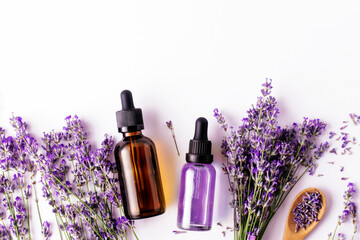 Bottled lavender essential oil and lavender sprigs on white background with copy space, top view. Spa concept.