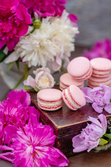 Obraz na płótnie Canvas Pink macaroons lie on a wooden box surrounded by peony flowers