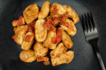 Aerial view of a close-up of Gnocchi with red sauce on a black plate. Accompanies a modern black fork.