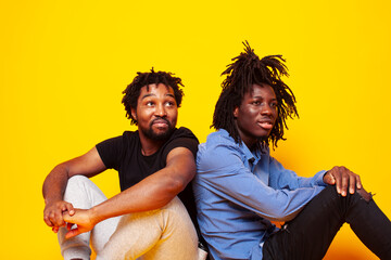Obraz premium two african american guys posing cheerful together on yellow background, lifestyle people concept