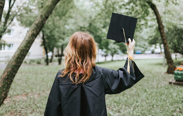 a middle-aged woman in the clothes of a graduate a coat and a cap celebrates the completion of...