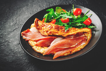 omelette with prosciutto and salad on black plate on Dark grey black slate background