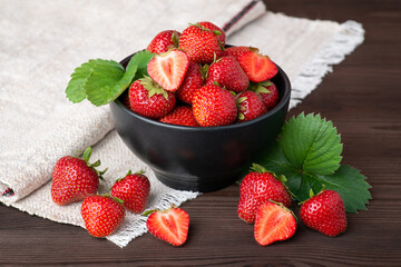 Beautiful composition with strawberry as a main object. Ripe red strawberries, some fresh green strawberry leaves on a dark wooden table with a towel behind