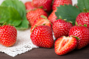 Close-up photo of delicious ripe strawberry on a table. Tasty fresh strawberries on a white linen kitchen towel with some leaves in the background