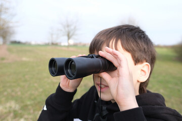 Fototapeta na wymiar boy, guy 8-10 years old stalker looks through black binoculars in the park, spies, hunts down secrets, the concept of surveillance, observation of people and animals
