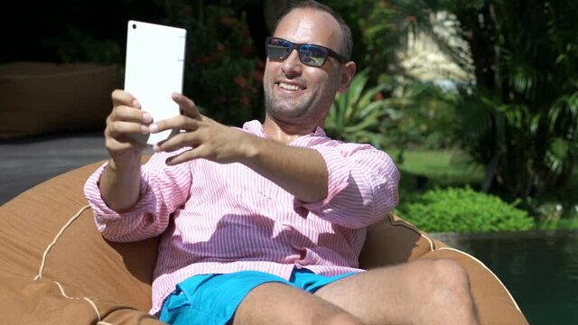 Young man taking selfie photo with smartphone by the pool