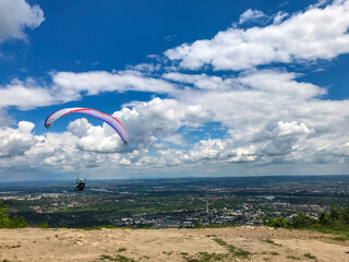 Paraglider taking off from the edge of the mountain over a city. Blue sky with clouds. Flying with a colordul parachute. Concept of freedom, relax, paragliding in the air