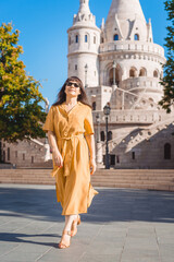 Solo traveler woman portrait. Stylish fashionable happy middle aged woman traveler wearing yellow dress walks in Fisherman Bastion in Budapest Hungary.
