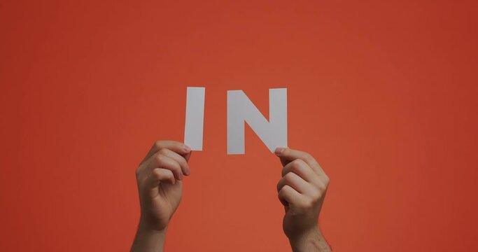 Hands raising up showing letters in of english language. Man shows preposition in made of carved paper