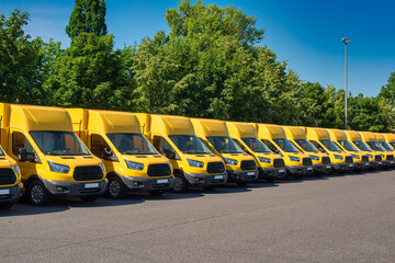 A lot of sustainable electric yellow delivery vans are parking in front of green trees.