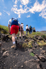 a Group of tourists with backpacks lined up along the trail on the background of mountains and blue sky.Every year thousands of tourists go to the mountains