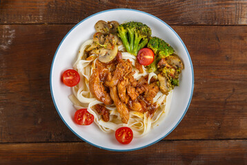 Udon with chicken in Japanese sauce and vegetables on a plate on a wooden table.
