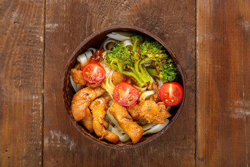 Udon with chicken in Japanese sauce and vegetables on a plate on a wooden table.