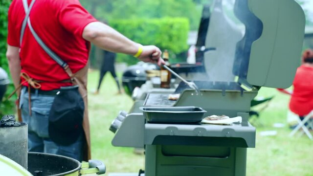 People celebrating weekend barbecue outdoors, man roasting assortment of meat on bbq grid and using cooking tongs for checking readiness of juicy meat. Barbecue picnic in nature