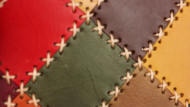 finger touches multi-colored patchwork leather surface with large stitching, quality test for craft, close-up view