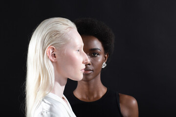 Caucasian albino girl and african american young woman portrait profile and full face on black background. Women friendship, love and relationships concept. - obrazy, fototapety, plakaty