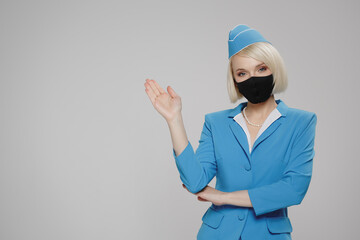 Attractive blonde stewardess in a protective mask points to an empty space. Gray background.