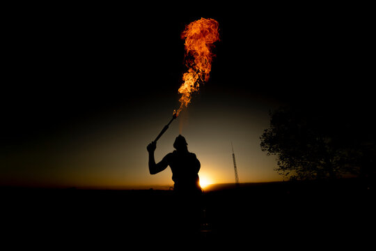 Fire-eater artist performing spit fire at sunset