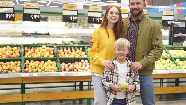 Happy caucasian family in supermarket aisle with cute kid boy, in casual wear, smile at camera.