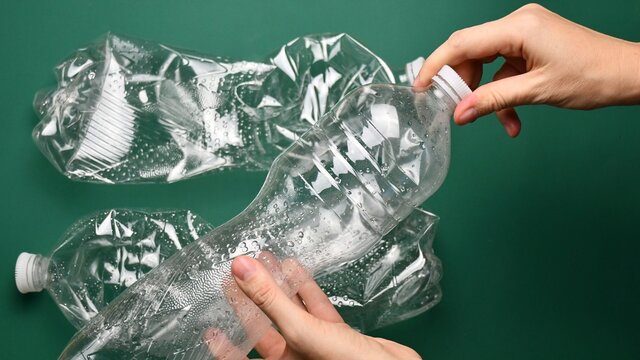 POV Female Hands Hold And Twist Cap Off From Transparent Pop Bottle For Separate Recycling. Empty Plastic Bottles On Green Background. First Point View Of Recycled Household Trash As Zero Waste