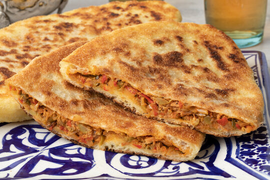 Pair of traditional fresh baked whole and halved Moroccan stuffed batbot  on a plate close up 