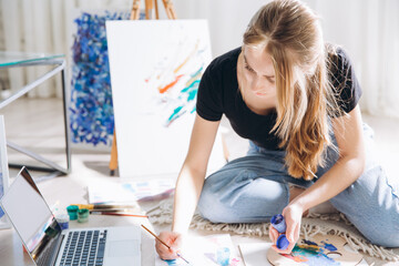 Smiling female artist paints picture on canvas with oil paints

