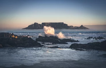 Photo sur Plexiglas Montagne de la Table Les vagues se brisent sur les rochers de la plage de Big Bay avec l& 39 emblématique Table Mountain en arrière-plan, Cape Town, Afrique du Sud.