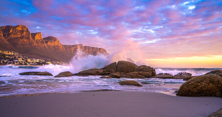 Fototapeta premium Beautiful sunset as waves crash on the rocks at Maiden's Cove beach, Camps Bay. The Twelve Apostles Mountain Range is where you'll find one of most scenic stretches of coast in the world