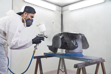 Male motorcyclist painting tank with spray gun in workshop