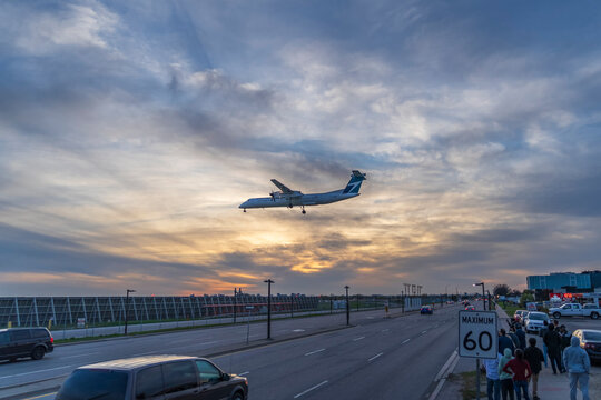 TORONTO, CANADA - MAY 12, 2018: C-GWEP WestJet Encore De Havilland Canada DHC-8-400 is landing over Airport Road at Toronto Lester B. Pearson Airport at sunset while people watching the landing 