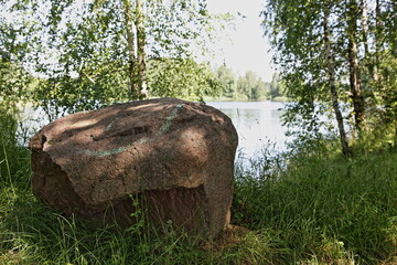 Large stone boulder near a beautiful wild lake at Sunny simmer day, ecological West Russian natural landscape