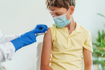 Fototapeta na wymiar doctor gives a child in a medical mask an injection in the shoulder. Vaccination of children against coronavirus. The vaccine against Covid-19