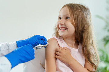 doctor gives a brave little girl an injection in shoulder. child is not afraid and smiles.Vaccination of children against coronavirus. vaccine against Covid-19. Close-up