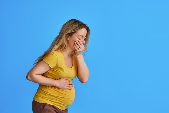 pregnant woman is tormented by morning sickness.. An unhappy expectant mother experiencing nausea feels very bad standing on a blue background. Gestosis and toxicosis in late pregnancy. Copy space