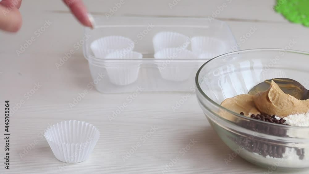 Wall mural A woman lays out paper candy tartlets. Next in a glass container are peanut butter, chocolate and coconut flour for cooking. Close-up shot.