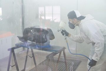 Male motorcyclist painting tank with spray gun in workshop