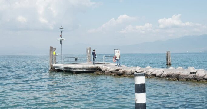 Two old friends waiting for the ferry on the Cisano pier, near Bardolino. Two men on Lake Garda look around. Summer in Veneto, German tourists in Italy.