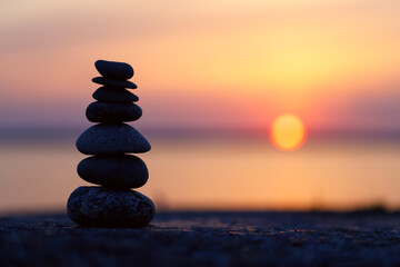 The stones of the pyramid balance on the rock at sunset. The background of the evening sea is blurred. Selective focus.