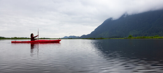 Adventure Caucasian Adult Woman Kayaking in Red Kayak surrounded by Canadian Mountain Landscape. Taken in Widgeon Valley, Pitt Meadows, Vancouver, British Columbia, Canada.