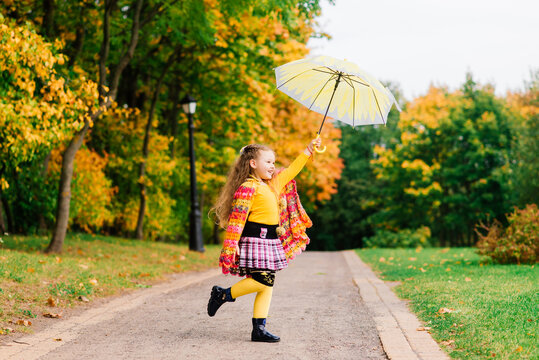 Smiling little girl with umbrella in raincoat and boots outdoor