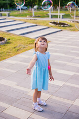 In a public park, a little girl blows and catches soap bubbles.The child is playing and laughing.