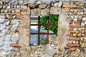 Antica vecchia finestra quadrata aperta ma con le sbarre, su vecchio muro di pietra  in rovina che guarda in un cortile interno.