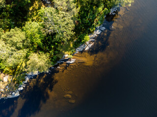 Bird's eye view of a pond, lake with green trees. Aerial, drone nature photography taken from above in Sweden in summer. Dark blue water surface background with copy space and place for text.