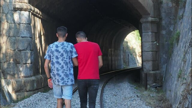 pareja de chicos caminando de espaldas entrando en un t&uacute;nel de ferrocarril cogidos de la mano en actitud muy cari&ntilde;osa