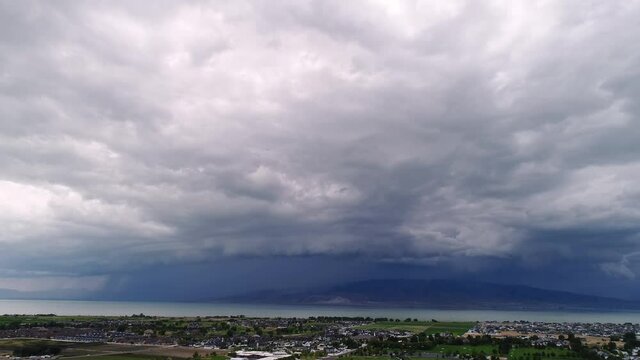 Aerial view flying over city as severe storm moves in over Utah Lake during hyperlapse.